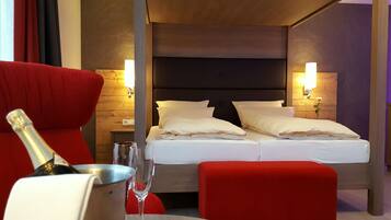 A hotel room with a bed, two bedside lamps, a red armchair, a small table with a bottle and glass, and a wooden headboard.
