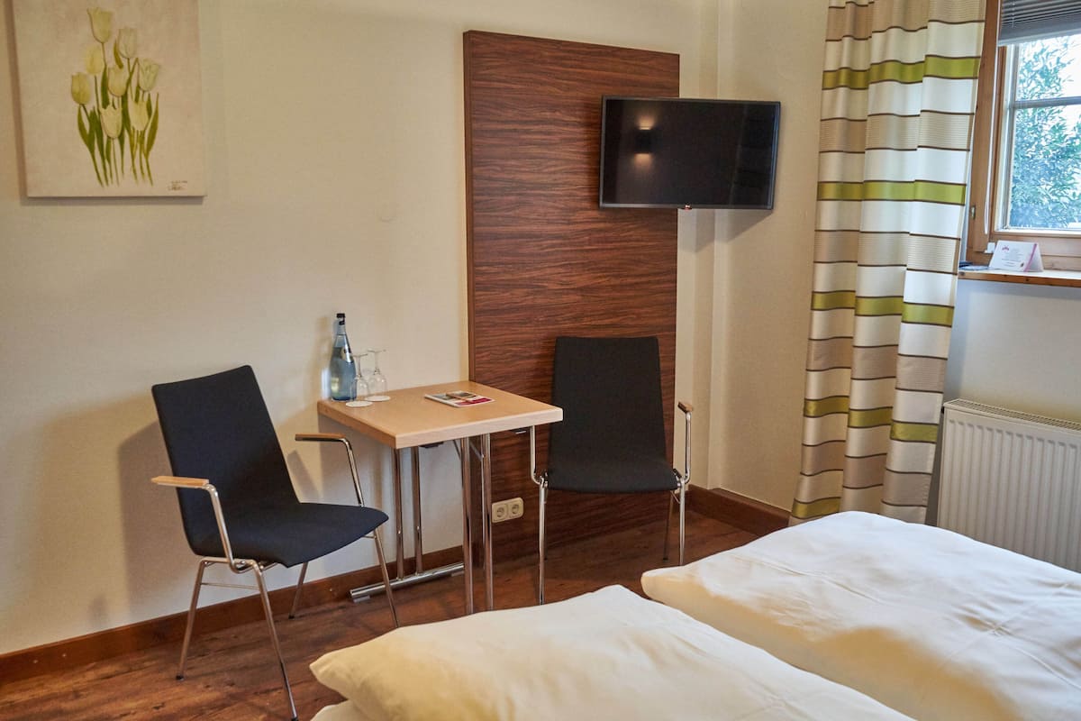 A hotel room with two beds, a TV mounted on the wall, a small table with chairs, and a window with curtains.