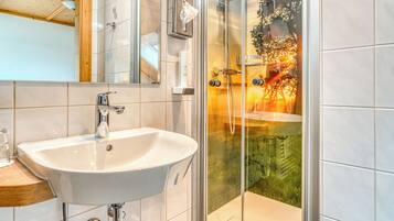 A modern bathroom with a white sink, a glass shower enclosure, and a wooden ceiling.