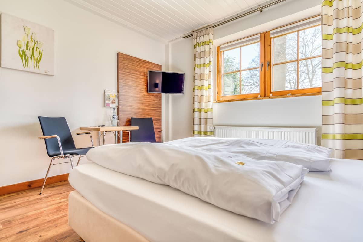 A hotel room with a bed, a desk, a chair, a TV, and a window with curtains.