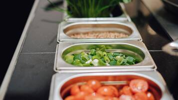 Een buffet met diverse gerechten, waaronder groene uien, tomaten en een bak geraspte kaas.