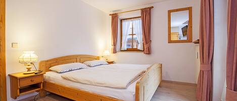 A bedroom with a wooden bed, bedside tables with lamps, a window with curtains, and a mirror on the wall.