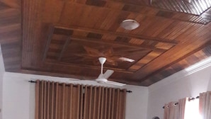 A living room with a ceiling fan, a black leather sofa, a wicker chair, and a wooden door. - Roo Neeroga (Marawila)