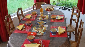 A dining table set for a meal with a view of a garden through a window. - Au Vieux Tilleul B&B (Les Trois Lacs)