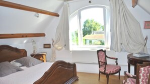 A bedroom with a wooden bed, a chair, a small table, and a window with curtains. - Au Vieux Tilleul B&B (Les Trois Lacs)