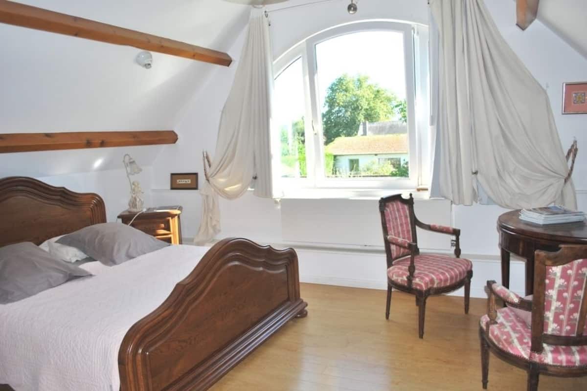 A bedroom with a wooden bed, a chair, a small table, and a window with curtains.