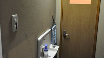 A small bathroom with a wooden door, a sink with a mirror, and a toilet sign on the wall.