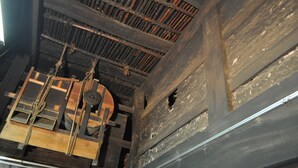 Ein Holzinnenraum mit einem großen Balkenbau, einem runden Holzgegenstand und einer Öffnung in der Wand.