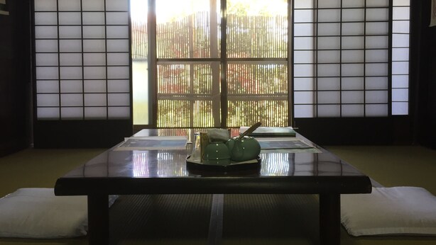 Ein traditioneller japanischer Raum mit Tatami-Boden, einem niedrigen Tisch mit einem grünen Keramik-Teeservice und Shoji-Schirmwänden.