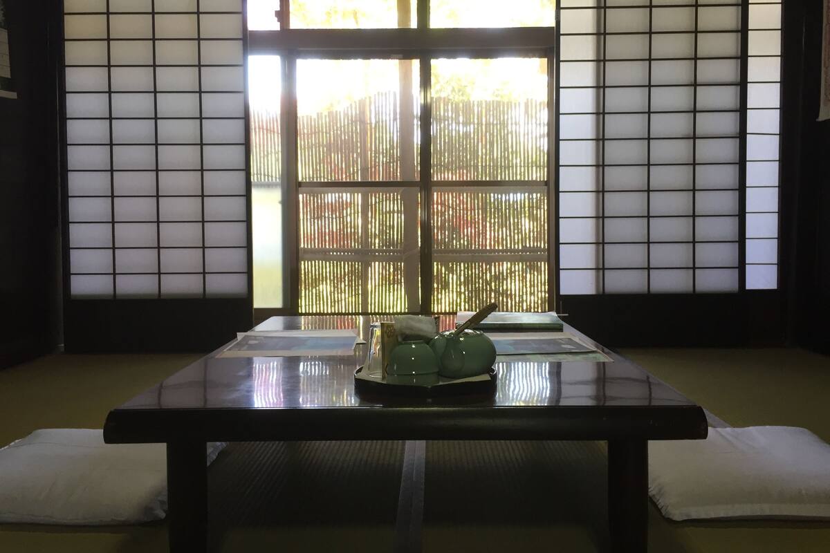 A traditional Japanese room with tatami flooring, a low table with a green ceramic tea set, and shoji screens.