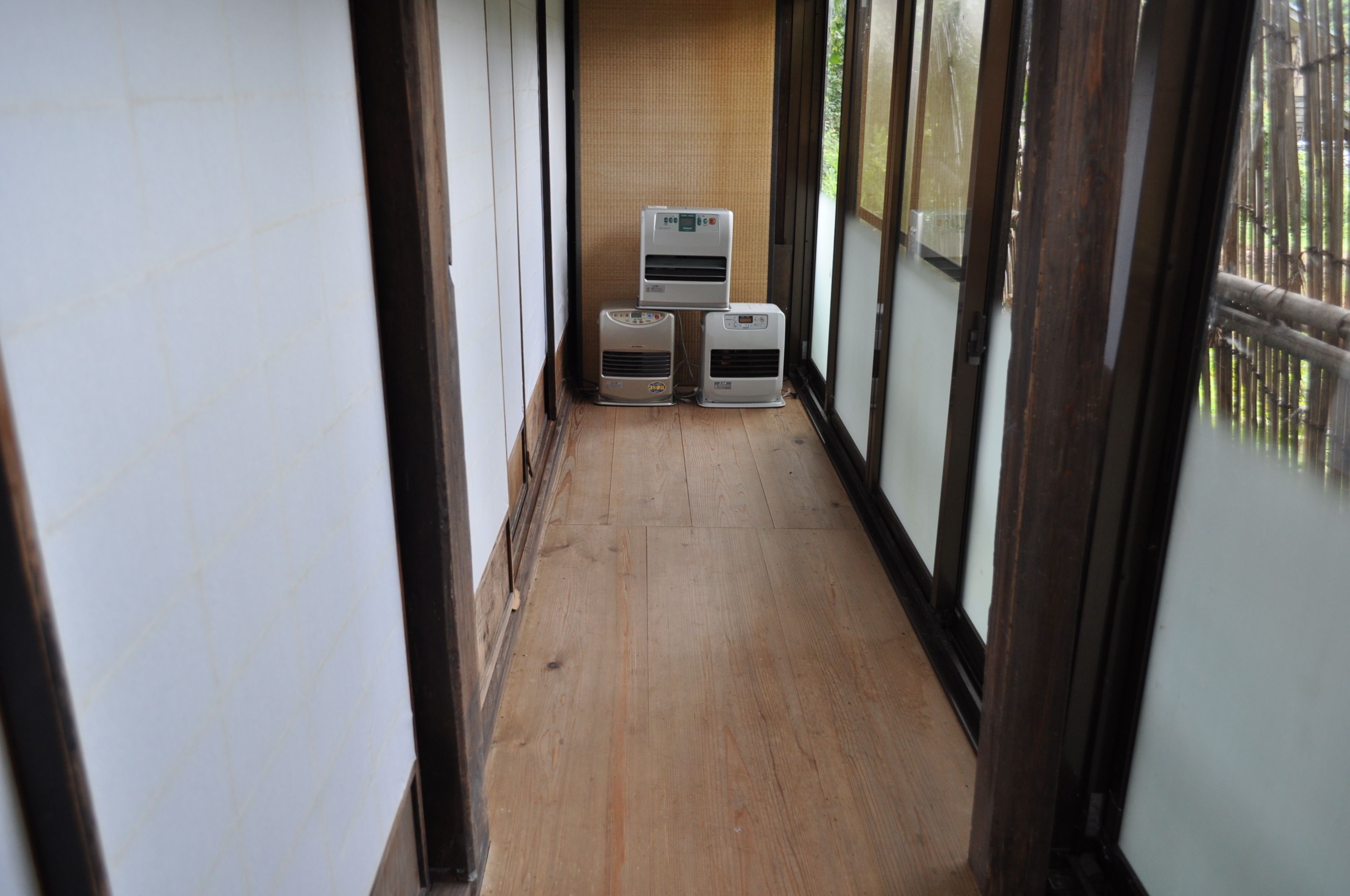 Un pasillo estrecho con suelo de madera y ventanas amplias en un lateral. Se observan tres unidades de aire acondicionado adosadas a la pared.