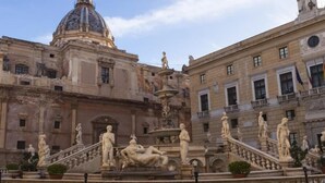 Un edificio histórico de arquitectura clásica, con una fuente central adornada con estatuas, una cúpula y una escalera con esculturas adicionales.