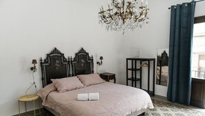 Una cama bien hecha con una colcha rosa y dos almohadas, un cabecero de madera oscura, una mesita de noche con una lámpara y un candelabro.