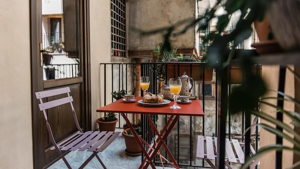Una pequeña mesa exterior con mantel rojo, dos sillas y una planta en maceta.