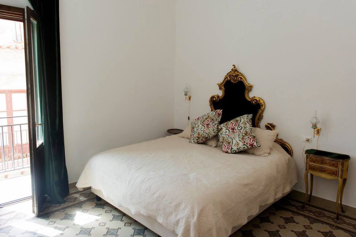 A bedroom with a bed, patterned pillows, a decorative headboard, a bedside table, and a lamp.