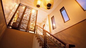 A staircase with a wooden handrail and a glass balustrade, leading to a landing with a decorative metal gate and two hanging lamps.
