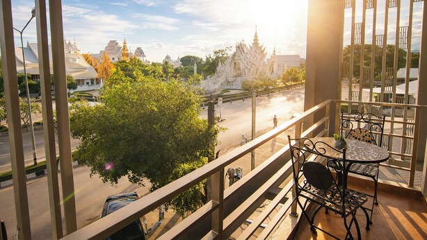 A balcony with a table and chairs, overlooking a street with trees and buildings.