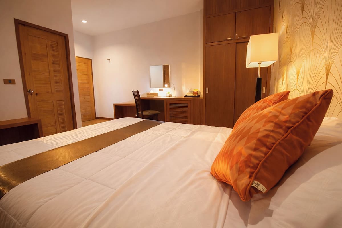 A hotel room with a bed, a desk, a chair, a lamp, and a wardrobe.