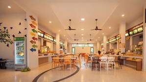 A spacious food court with multiple seating areas, ceiling fans, and a variety of food display counters.