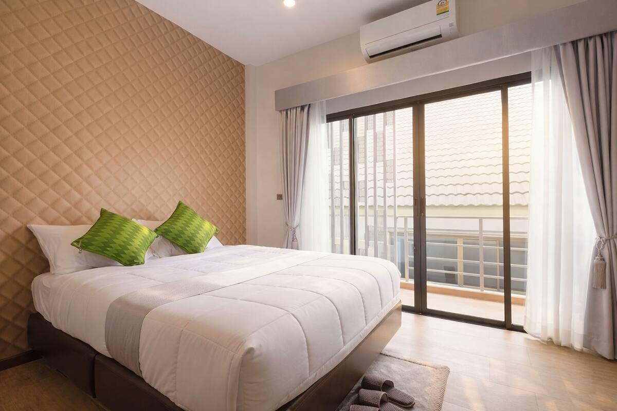 A bedroom with a large bed, a quilted wall, a sliding glass door to a balcony, and an air conditioning unit.