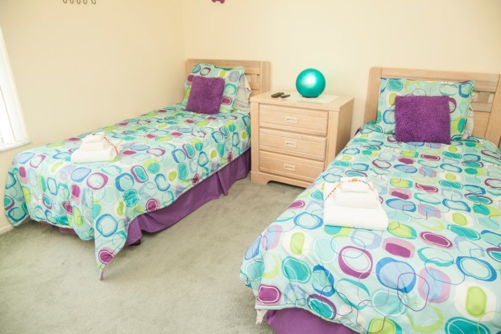 A room with two single beds, each with a colorful circular-patterned bedspread and a purple pillow. There is a wooden nightstand with a teal ball and a pair of sunglasses on it.