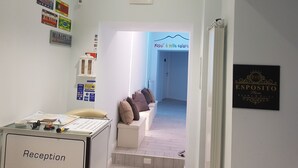 Un área de recepción con un cartel de bienvenida a los huéspedes en varios idiomas, un mostrador de recepción y vistas a una sala con sofá y cojines.