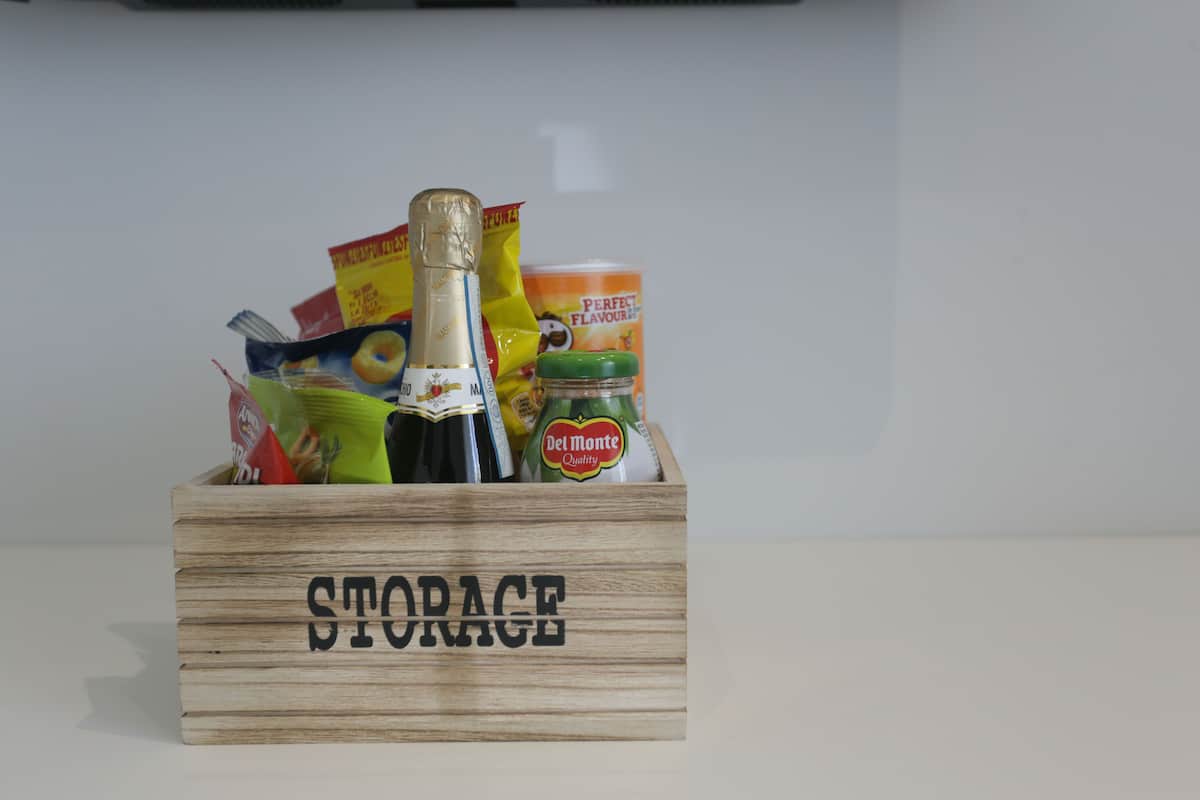 Een houten doos met de tekst 'STORAGE', gevuld met verschillende etenswaren en een fles Del Monte.