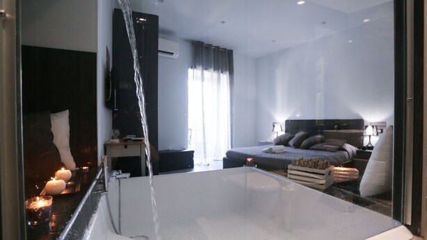 Un dormitorio moderno con una cama grande, una mesita de noche, un televisor y una bañera con agua fluyendo.