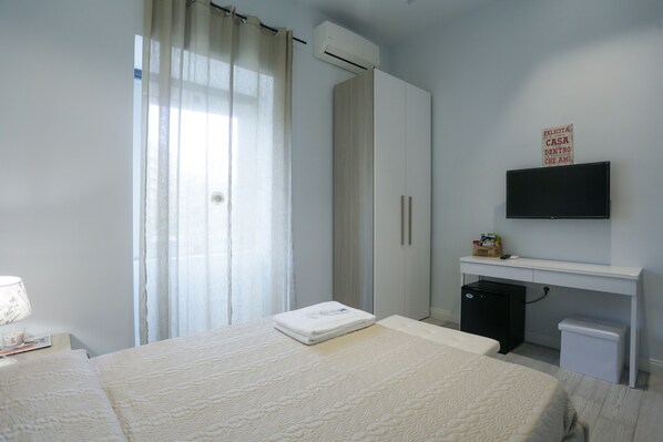 A hotel room with a bed, a desk with a computer, a TV, and a small fridge. - Esposito Plaza - Rooms & Suite (Naples)