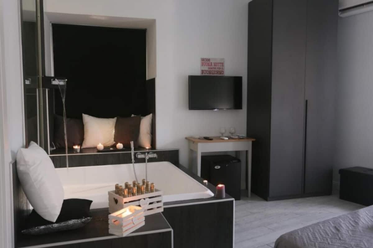 Een moderne slaapkamer met een groot bed, een nachtkastje met kaarsen, een aan de muur bevestigde televisie en een donkere kast.