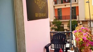 Un balcón con una mesa para dos, una silla y una maceta con flores rosas.