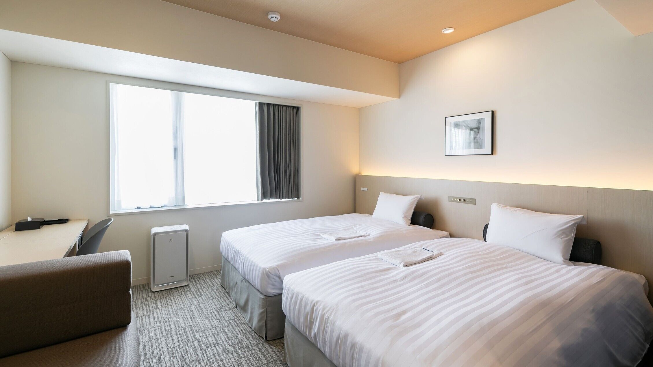 A hotel room with two beds, a desk, a chair, a radiator, and a window with curtains.