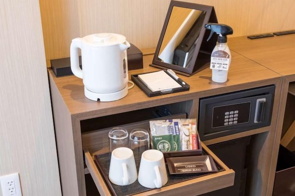 A hotel room's kitchenette with a coffee maker, a digital scale, a coffee pod dispenser, and a tray with coffee cups and a coffee maker.