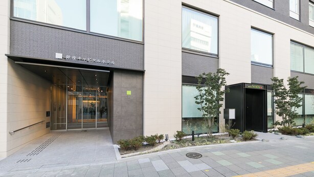 A modern building with a glass entrance, a sign reading "KURIA," and a small garden area with plants. - Ginza Capital Hotel Moegi (Tokyo)