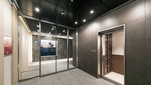 A modern elevator interior with glass doors, a digital display, and a wooden panel. - Ginza Capital Hotel Moegi (Tokyo)