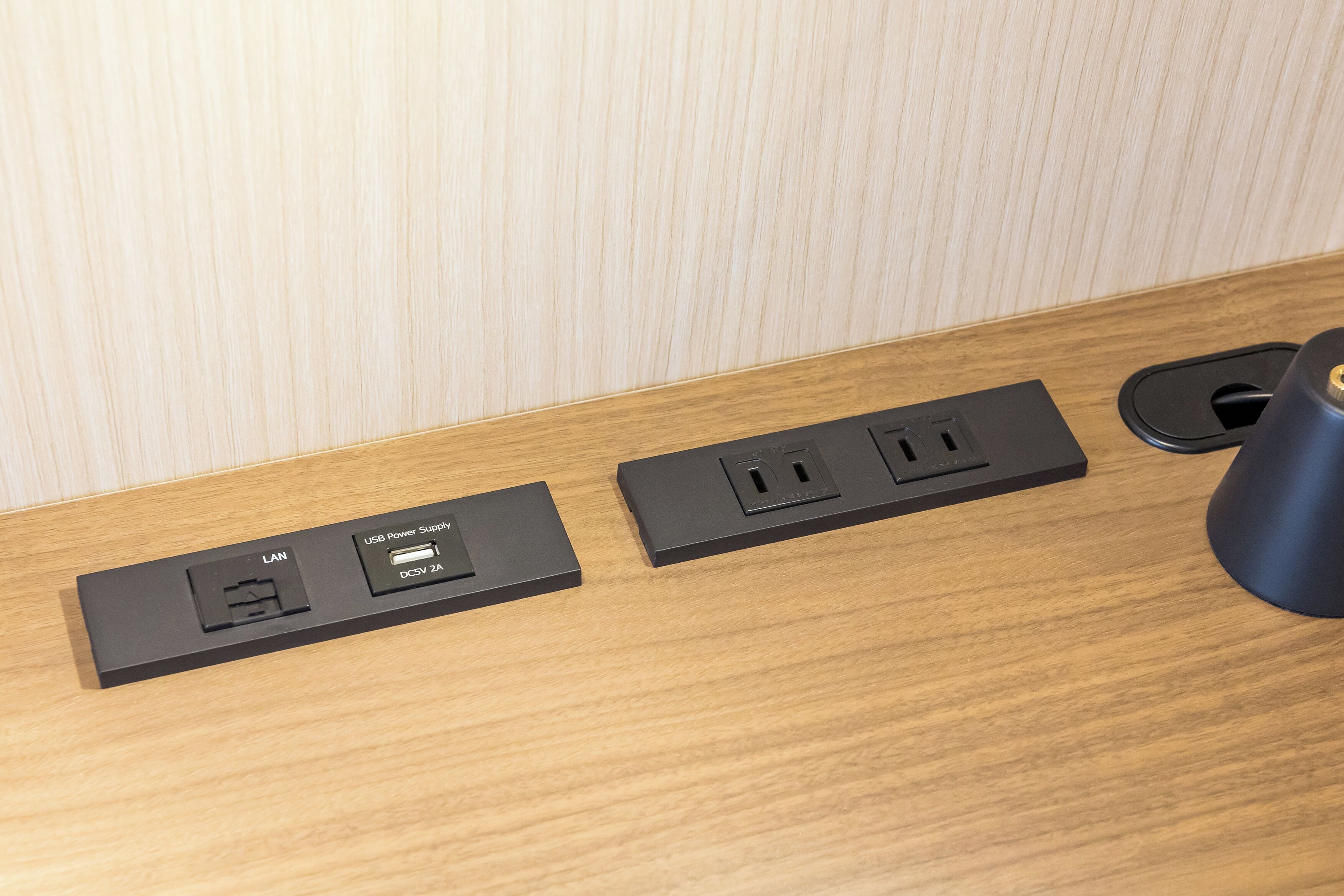 A wooden surface with two black power strips, one with a LAN port and USB power supply, and another with a standard outlet.