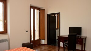 Habitación de hotel con cama, escritorio y silla, televisión y puerta que da a un balcón.