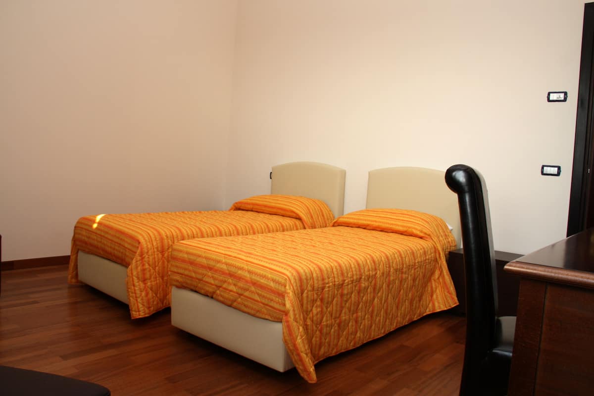 A room with two beds, wooden flooring, and a black chair.