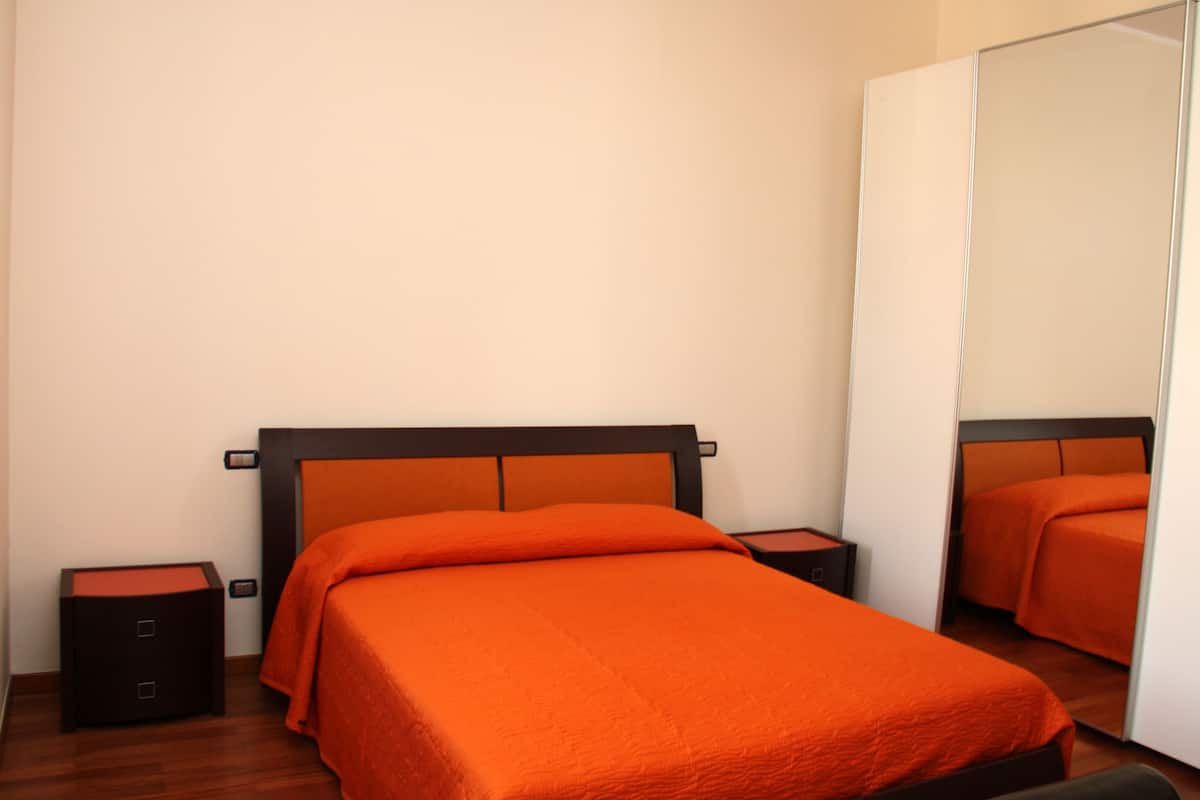 A bedroom with a bed, nightstands, and a large mirror.