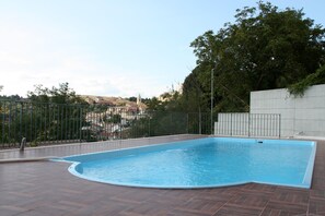 An outdoor swimming pool with a curved edge, surrounded by a metal fence and a concrete wall. - Affittacamere Bellavista (San Marco dei Cavoti)