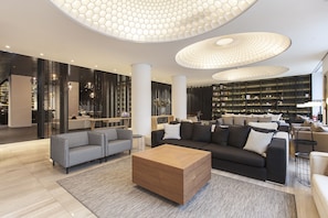 Relax in this inviting living area with a central coffee table, comfortable sofas, and a bookshelf filled with books and decorative items.