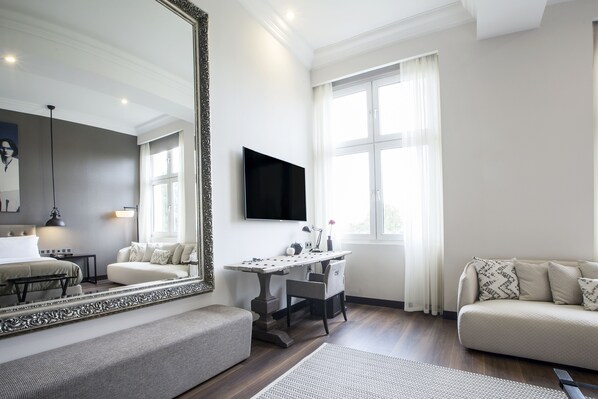Ein modernes Wohnzimmer mit großem Spiegel, Flachbildfernseher, Sofa, Schreibtisch und Sessel.