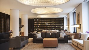 Ein modernes Wohnzimmer mit einer schwarz-weißen Sofagarnitur, einem Holztisch und einem großen Bücherregal, voll mit Büchern.