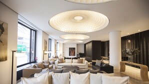 Eine moderne Lobby mit einer zentralen Sitzgruppe, großen Fenstern und einem markanten Deckenstil.