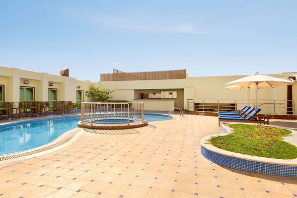 Un área de piscina con un jacuzzi circular, sillas de descanso y una zona de estar cubierta.