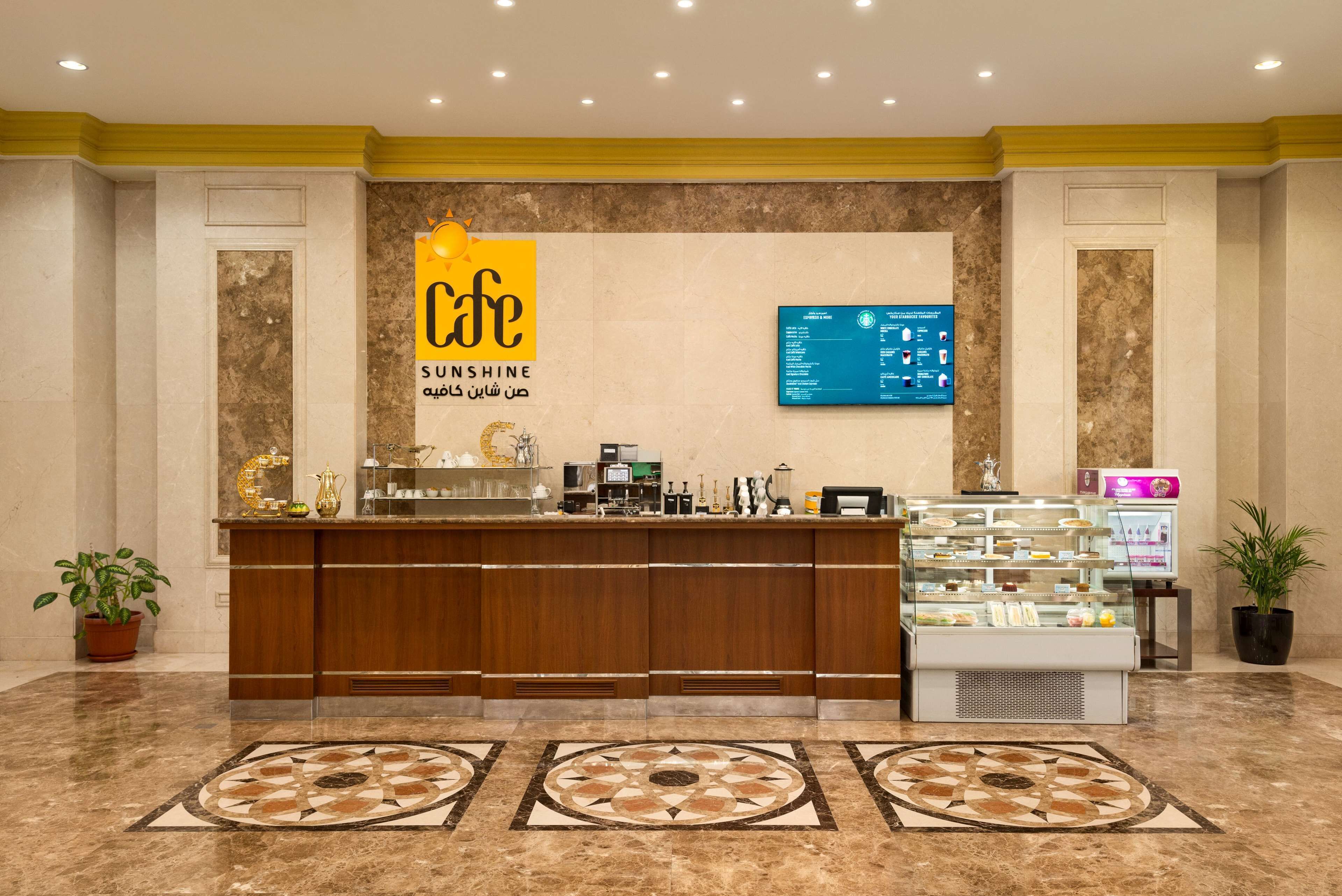 A reception area with a marble floor, a wooden reception desk, a glass display case with desserts, and a digital screen above the desk.