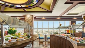 A breakfast buffet with a variety of food items, a seating area with chairs, and a view of the city through large windows.