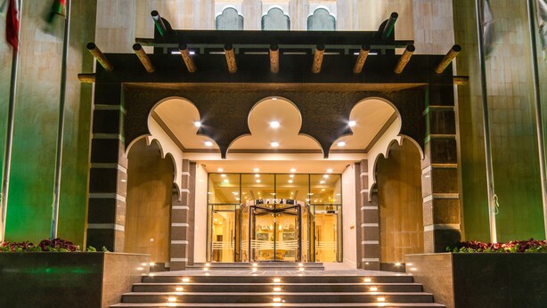 A hotel entrance with a grand staircase, a revolving door, and a decorative archway.