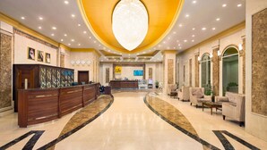 A hotel lobby with a reception desk, seating area, and a large chandelier.
