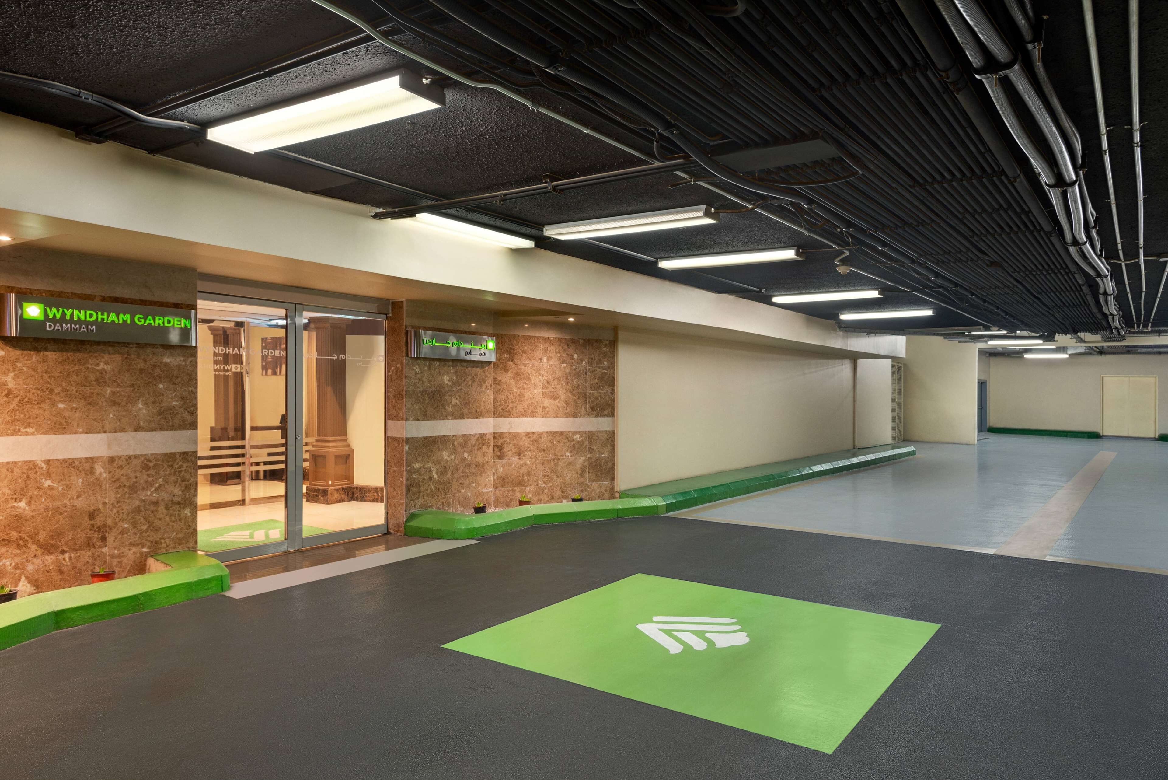 A modern indoor space with a green carpet area, a sign for 'Wyndham Garden', and a marble wall.
